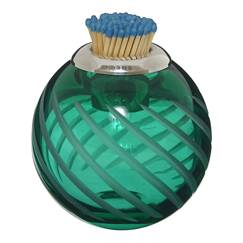 An emerald, green, round crystal glass with diagonal cuts with a silver holder for blue-tipped matches that sits on the top of the glass.